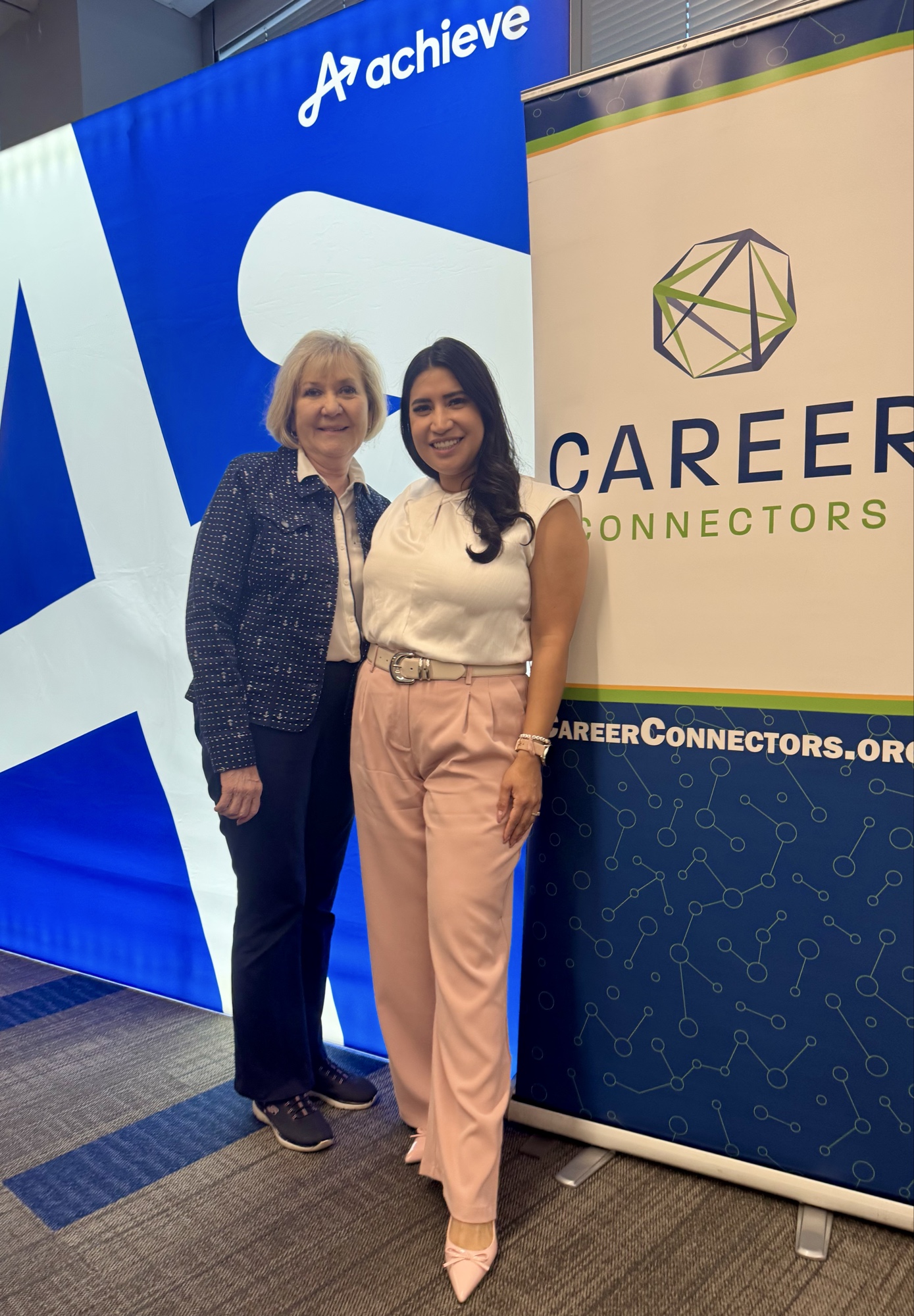 Linda Luman (Curriculum Lead) with Martha Mauer (KTAR News, 2025 keynote speaker) between the Career Connectors and Achieve banners at the 2025 Inspired LeadHER event.