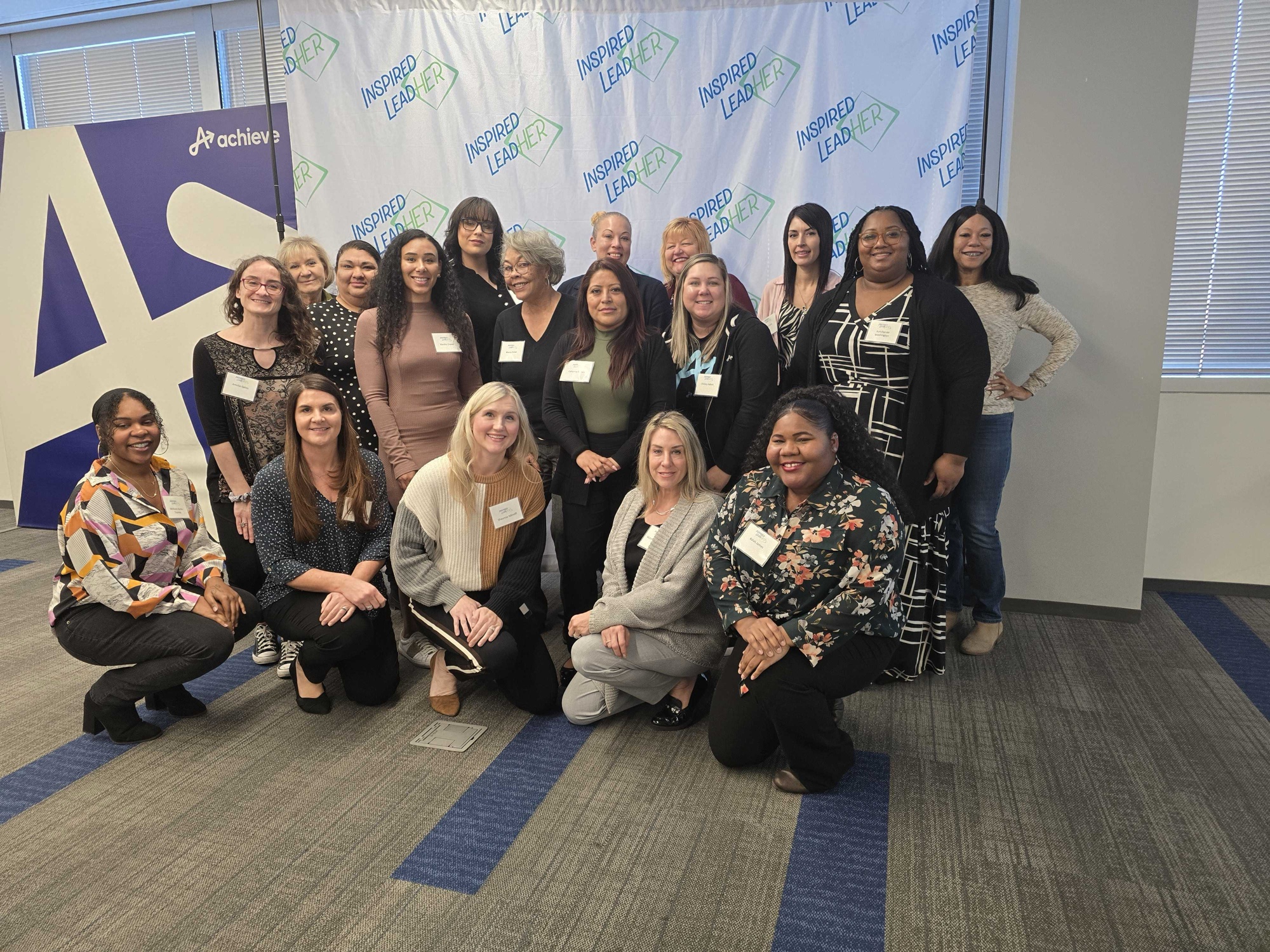 The full 2025 Inspired LeadHER cohort posed in front of the Inspired LeadHER step-and-repeat backdrop and Achieve campus signage in Tempe, Arizona.