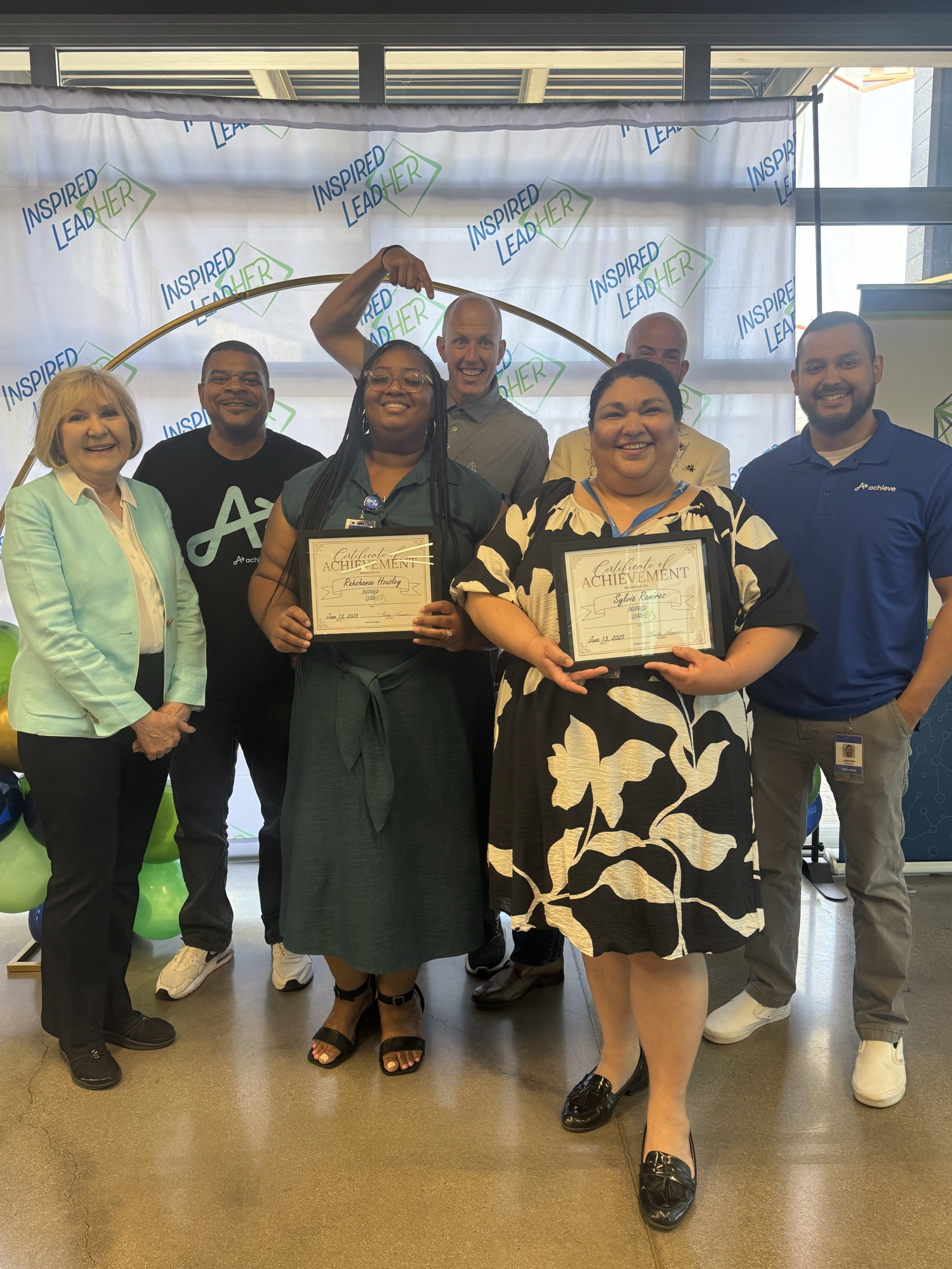 Two Inspired LeadHER 2025 graduates holding certificates surrounded by Achieve partnership team members at graduation.