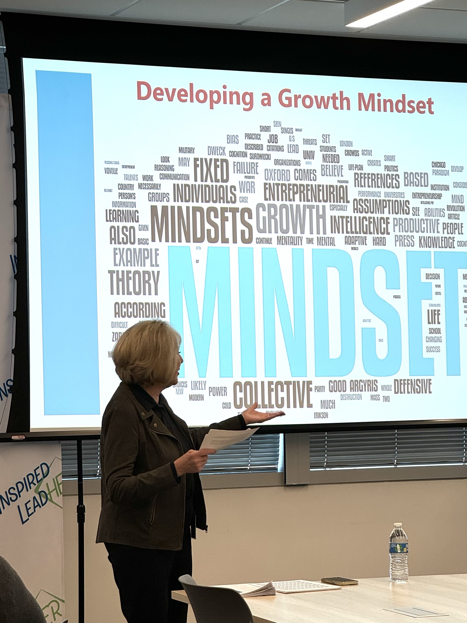Linda Luman, Curriculum Lead, leading the Developing a Growth Mindset session in front of the program word cloud slide and Inspired LeadHER backdrop.
