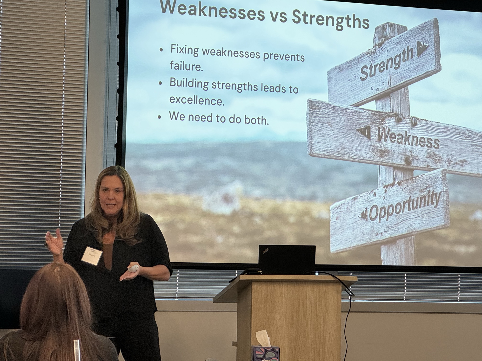 A speaker presenting a Weaknesses versus Strengths comparison slide during a 2025 Inspired LeadHER cohort session.